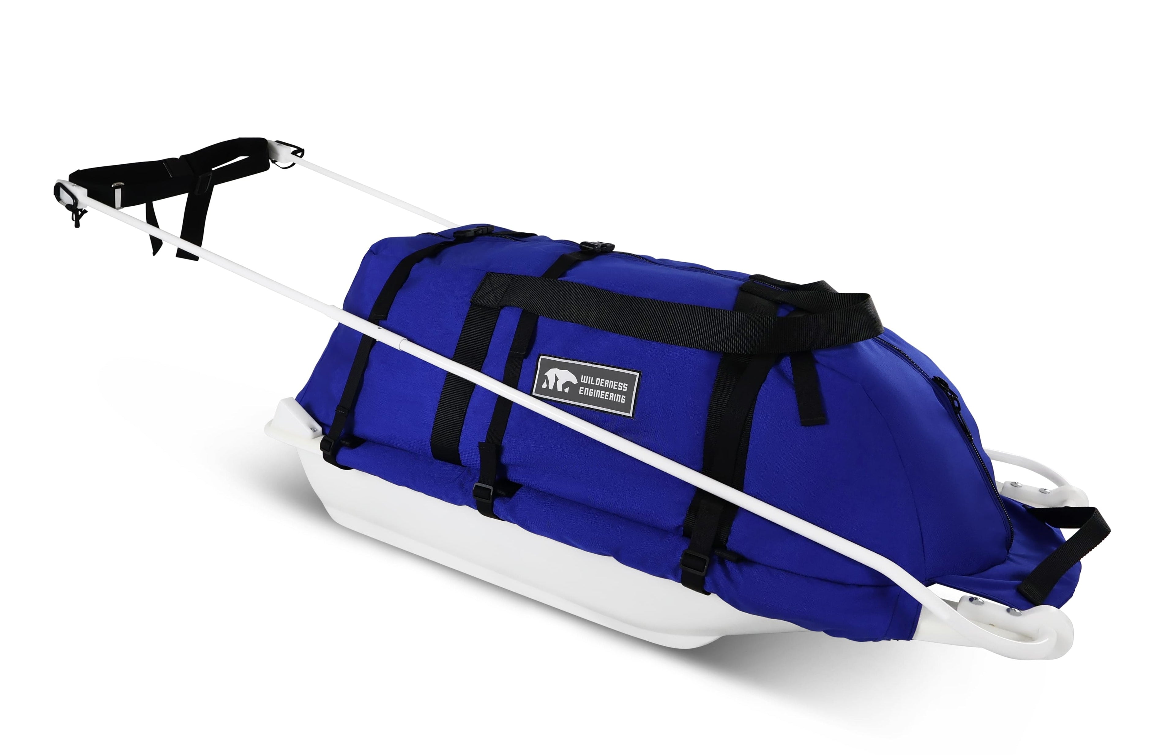 A Royal Blue snowmobile Sled Pulk cargo bag with black straps and a white plastic base, shown on a white studio background. With a tag labeled 'Wilderness Engineering'.