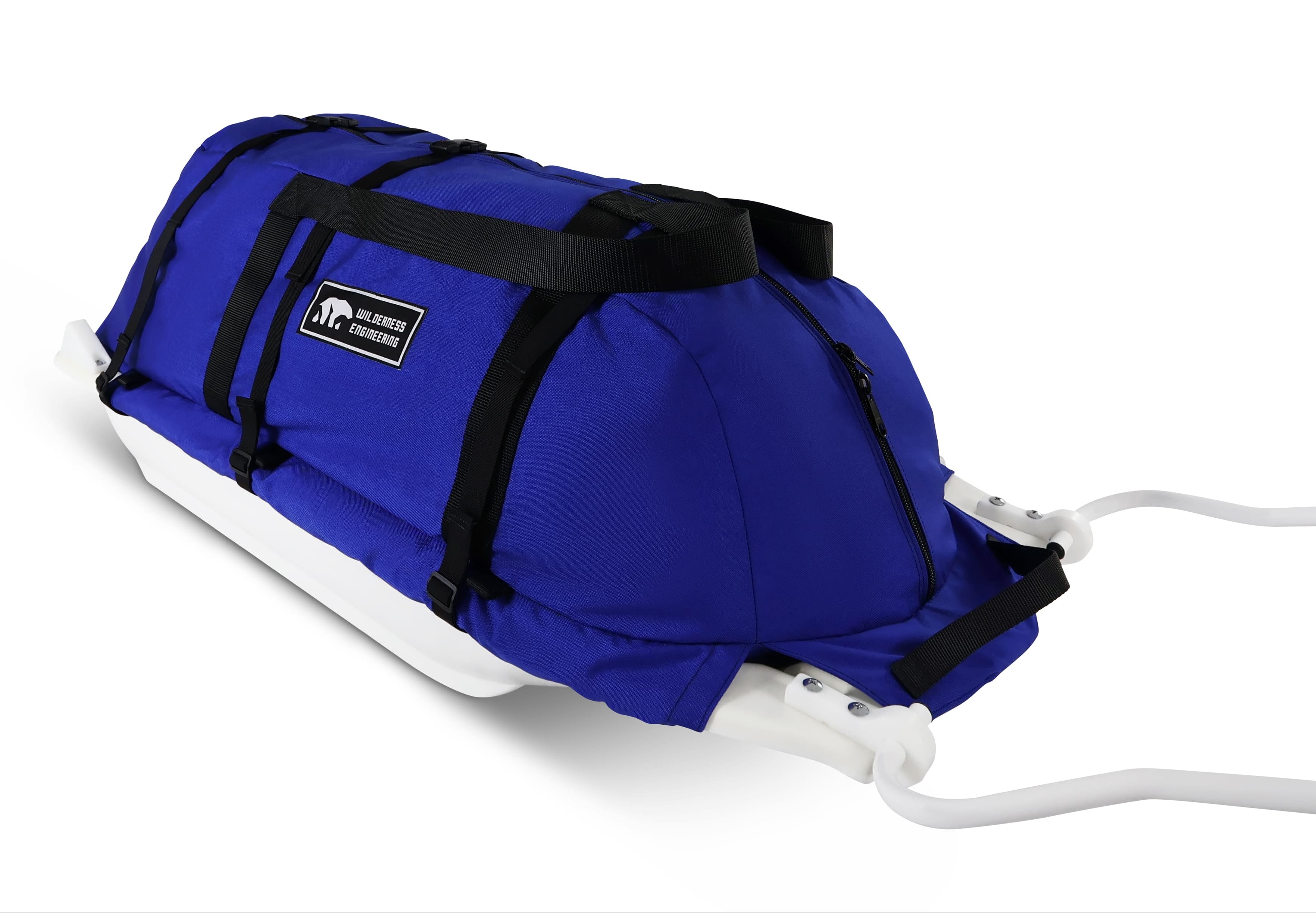 A Royal Blue snowmobile Sled Pulk cargo bag with black straps and a white plastic base, shown on a white studio background. With a tag labeled 'Wilderness Engineering'.