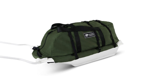 A Olive Green snowmobile Sled Pulk cargo bag with black straps and a white plastic base, shown on a white studio background. With a tag labeled 'Wilderness Engineering'.