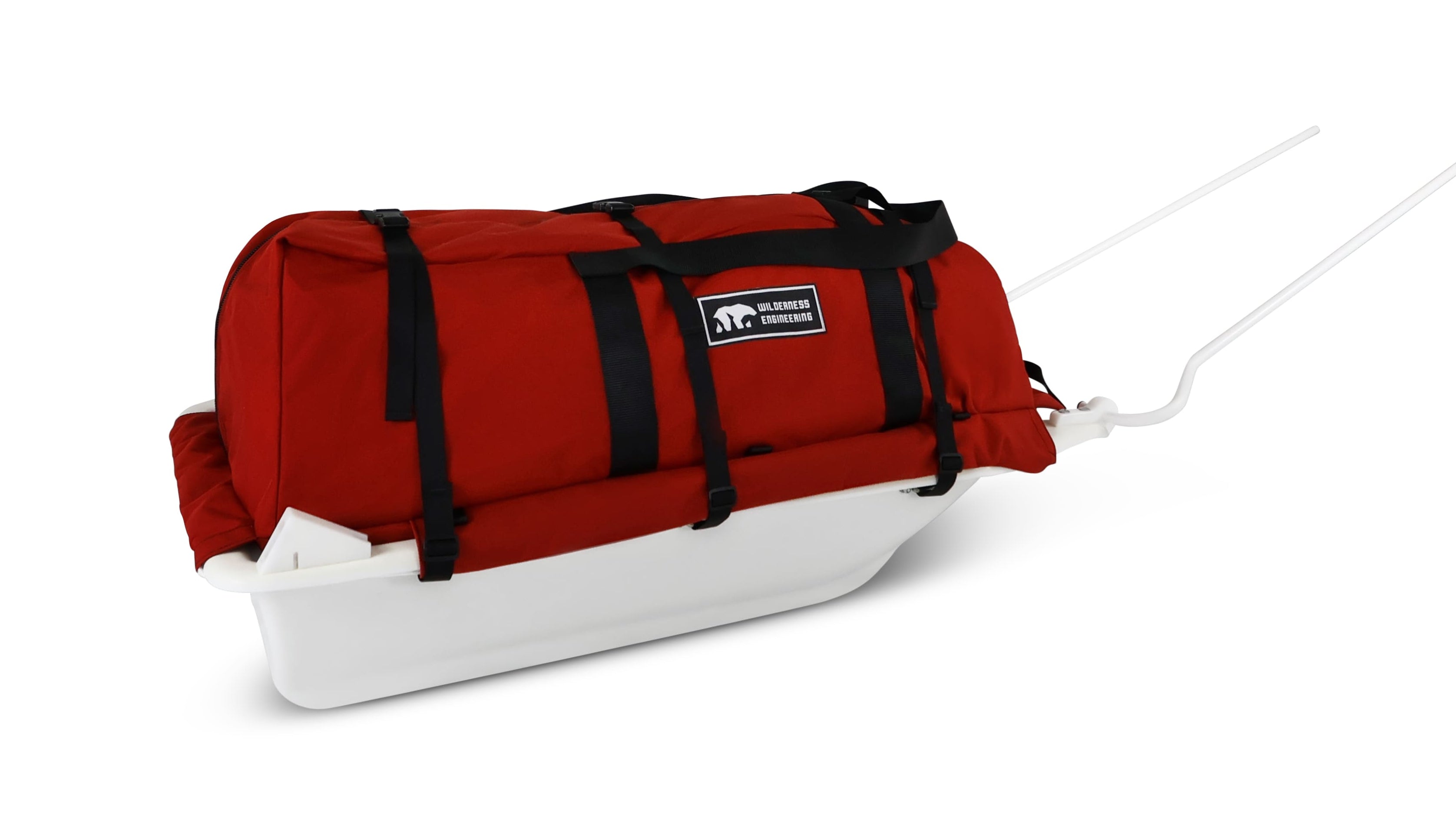 A Red snowmobile Sled Pulk cargo bag with black straps and a white plastic base, shown on a white studio background. With a tag labeled 'Wilderness Engineering'.