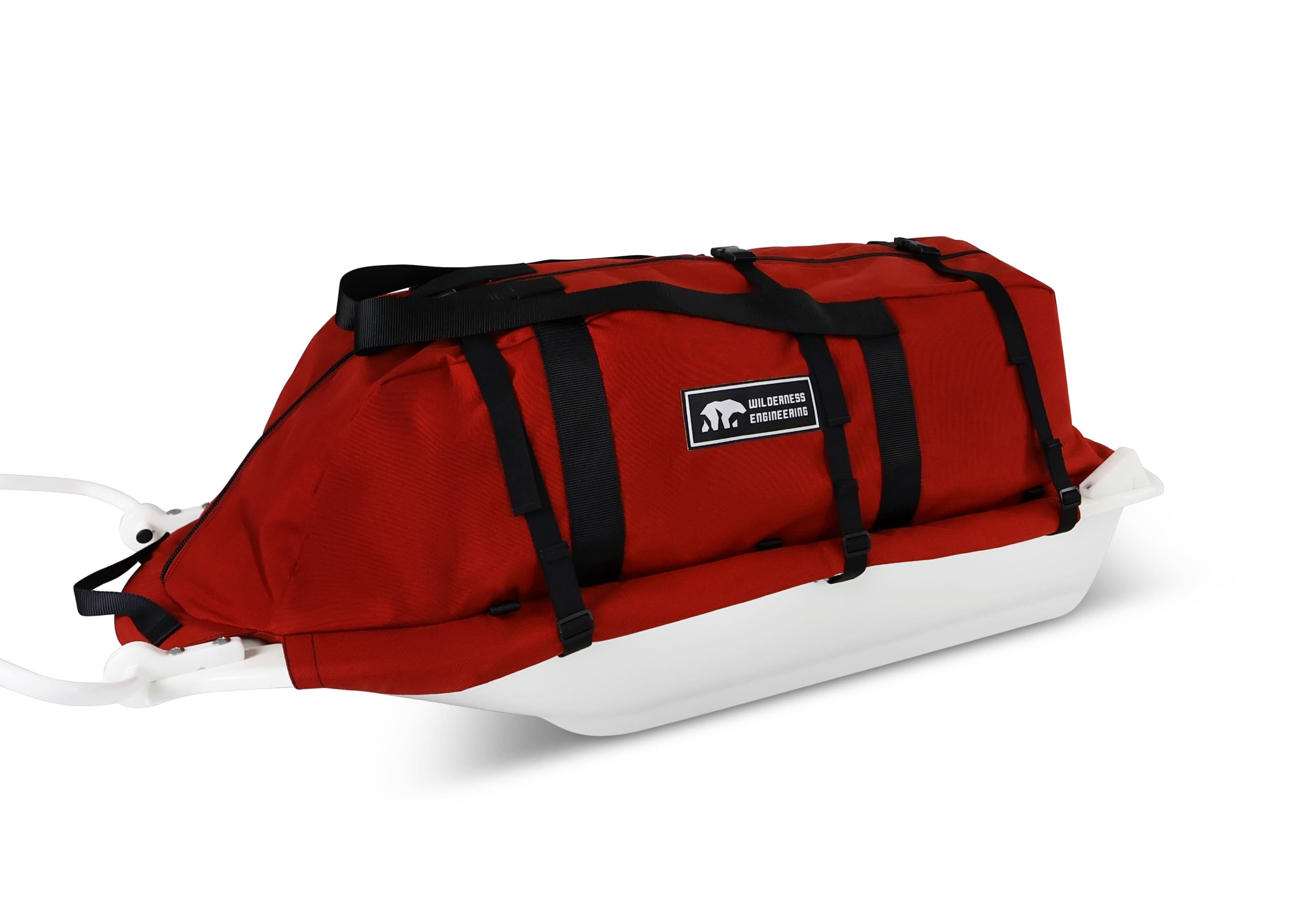 A Red snowmobile Sled Pulk cargo bag with black straps and a white plastic base, shown on a white studio background. With a tag labeled 'Wilderness Engineering'.