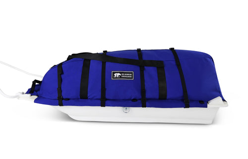A blue snowmobile pulk sled cargo bag with black straps and a white plastic sled base, shown on a clean white background. A black label on the front displays the brand 'Wilderness Engineering'.