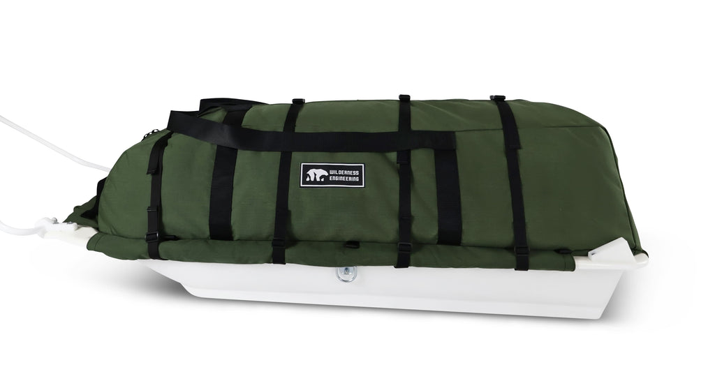A Olive Green snowmobile pulk sled cargo bag with black straps and a white plastic sled base, shown on a clean white background. A black label on the front displays the brand 'Wilderness Engineering'.