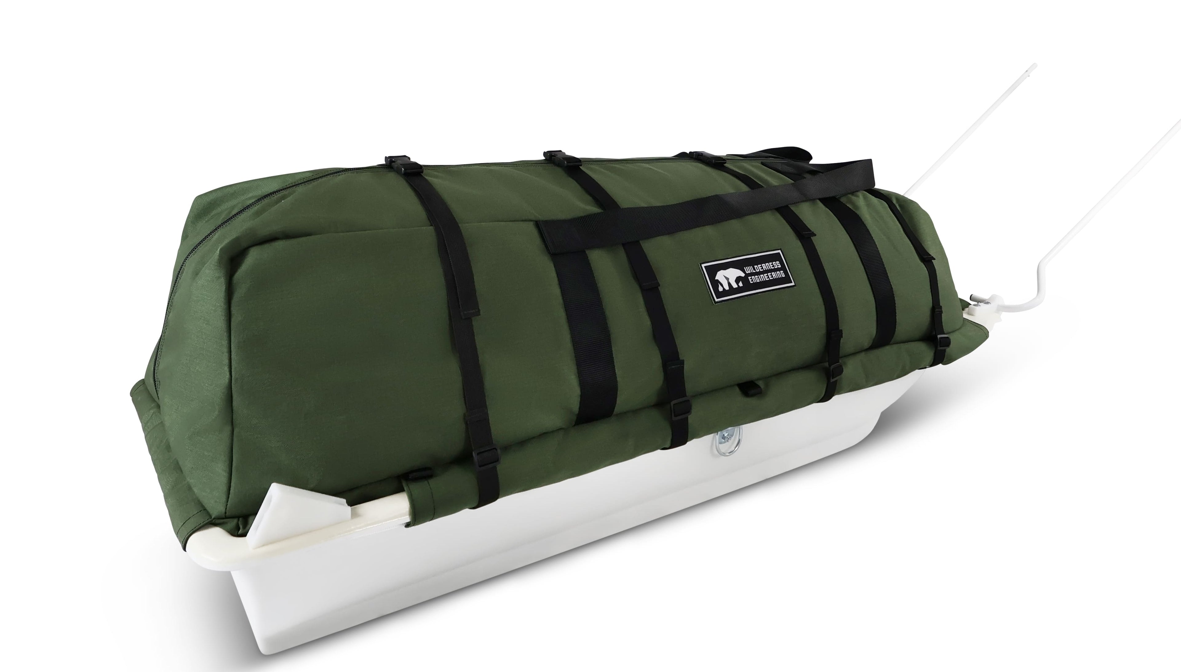 An olive green snowmobile cargo bag with black straps and a white plastic base, shown on a white studio background. With a tag labeled 'Wilderness Engineering'.