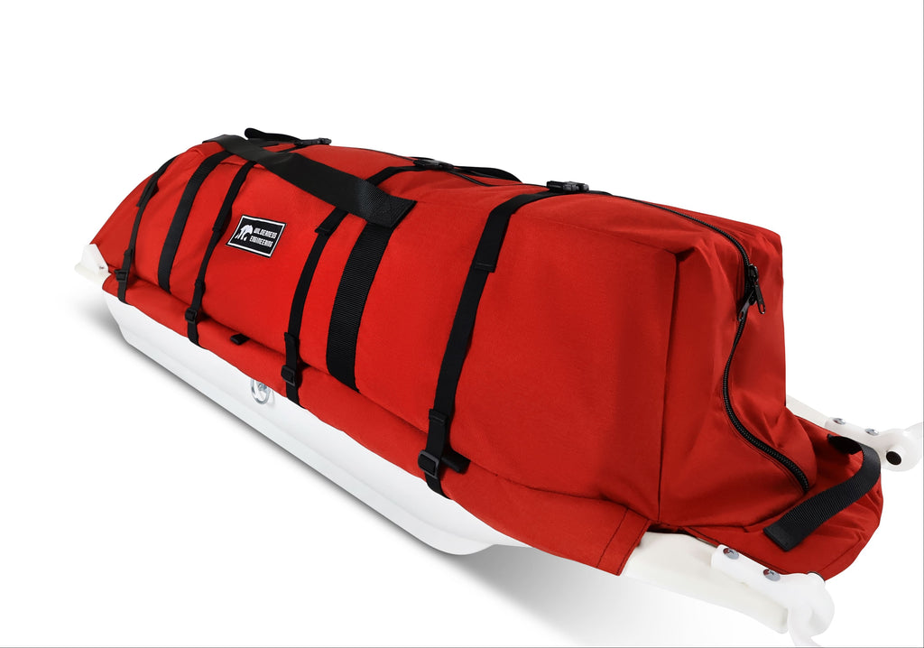 An Red snowmobile Sled Pulk cargo bag with black straps and a white plastic base, shown on a white studio background. With a tag labeled 'Wilderness Engineering'.