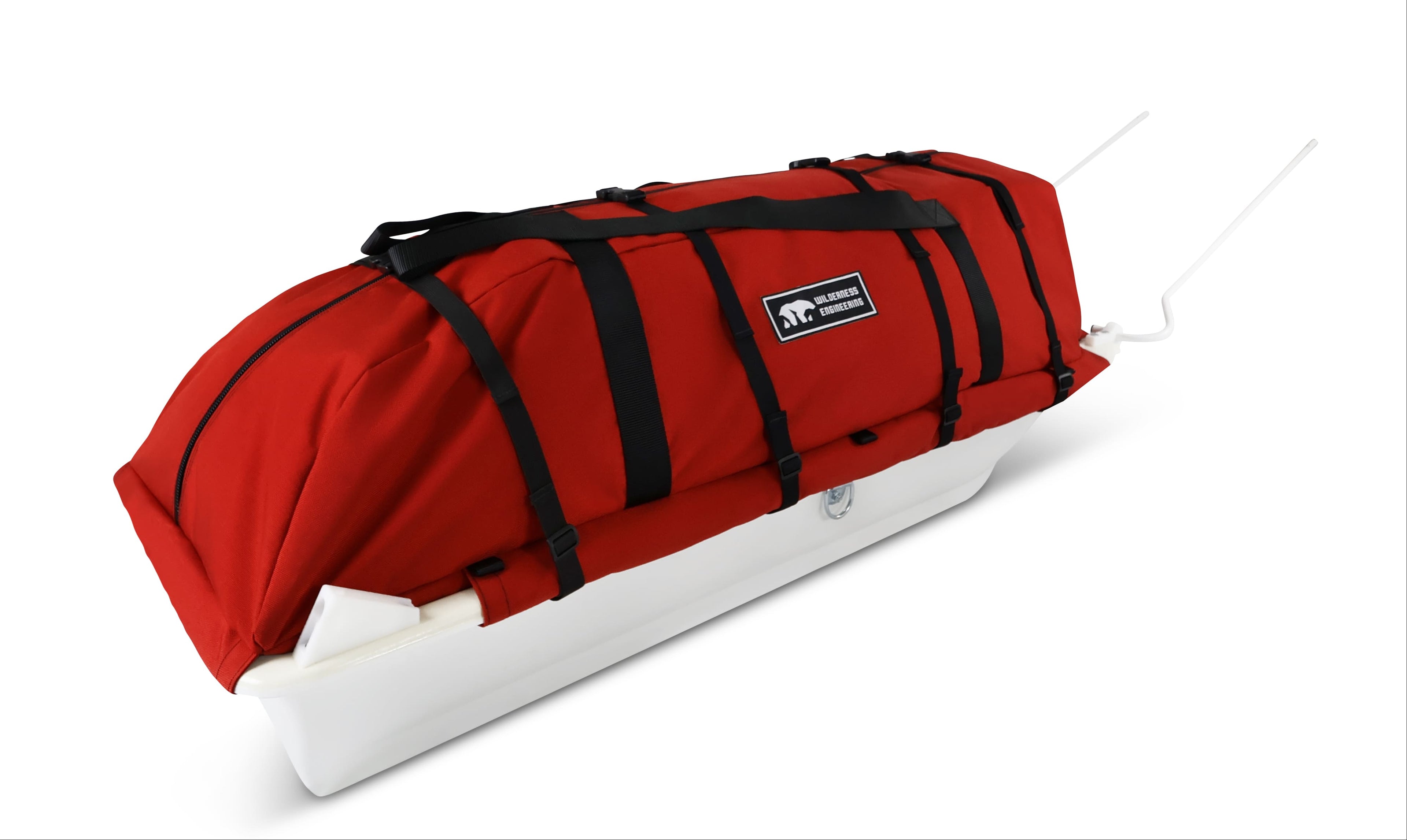 An Red snowmobile Sled Pulk cargo bag with black straps and a white plastic base, shown on a white studio background. With a tag labeled 'Wilderness Engineering'.